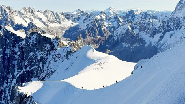 Paragliders with backpacks descend the steep snowy slopes of Aiguille du Midi, Chamonix, preparing for a parachute jump between the majestic peaks of the French Alps, with aamazing view of Mont Blanc