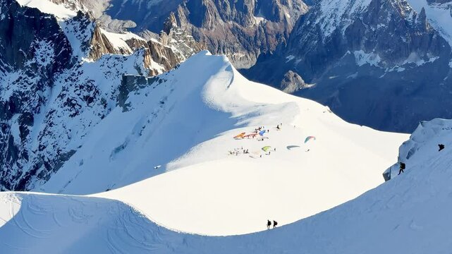 Paragliders with backpacks descend the steep snowy slopes of Aiguille du Midi, Chamonix, preparing for a parachute jump between the majestic peaks of the French Alps, with aamazing view of Mont Blanc