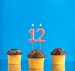 Three birthday cupcakes with number 12 candle - Blue background.