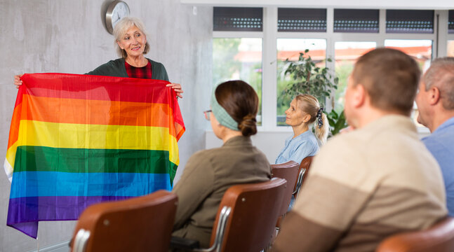 Mature female professor showing flag of lgbt pride to elderly students