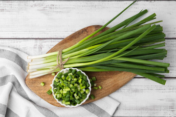 Chopped green onion in bowl and stems on white wooden table, top view