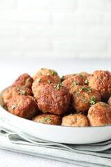 Tasty cooked meatballs with green onion in bowl on white table, closeup