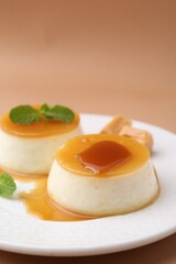 Tasty puddings with caramel sauce served on light brown background, closeup