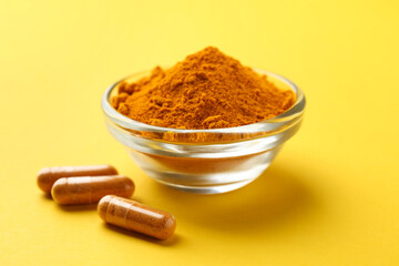 Turmeric powder in bowl and capsules on yellow background, closeup