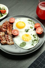 Tasty brunch. Delicious fried eggs, bacon, tomatoes and juice served on black table, closeup