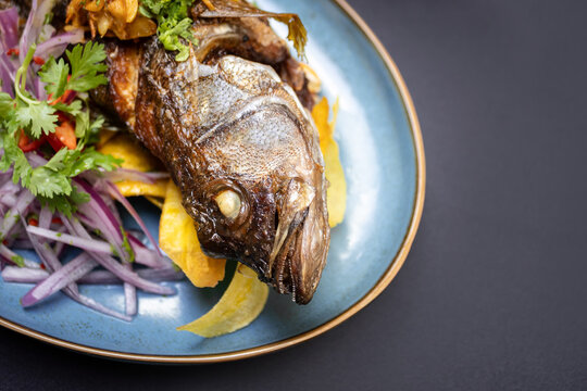 Pescado cabrilla frito crujiente y dorado, servido con lim&oacute;n  con cebolla y chifles 