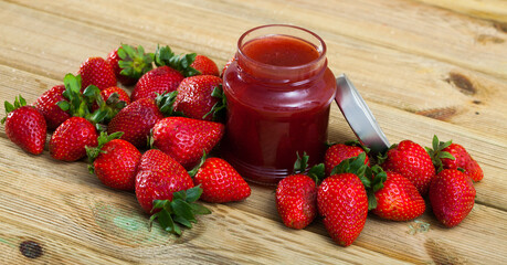 Healthy vitamin dessert. Ripe berries of fresh sweet strawberry and jar of jam on wooden table..