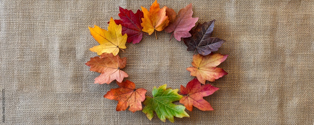 Aufkleber Colorful autumn maple leaves arranged in a circle on a burlap cloth, creating a rustic and natural fall backdrop