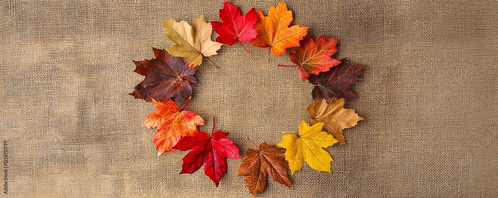 Poster Circle of colorful autumn maple leaves arranged on a burlap background, creating a beautiful fall-themed image