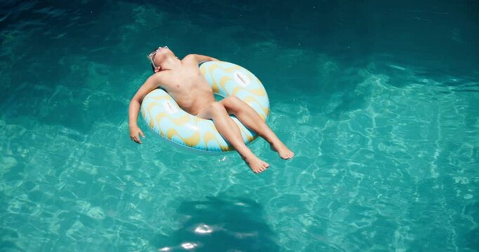 Boy, donut and kid floating in pool water, freedom and summer break for peace on vacation. Child development, inflatable support and chilling on holiday trip, travel and hotel facility to relax