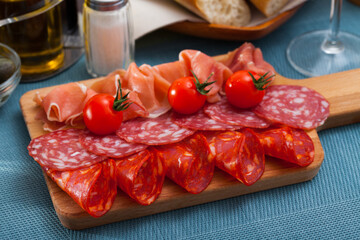 Spanish tasty meal slicing sausages and jamon with tomatoes at wooden desk, close up