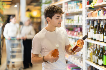 Young male customer in supermarket examines bottles of wine, chooses alcoholic drink. Attentive...