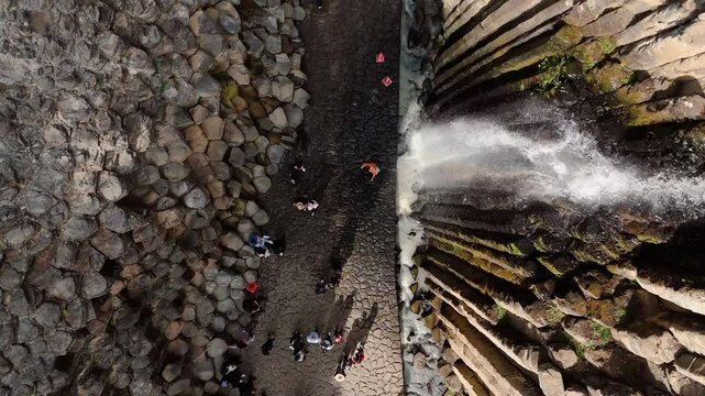 People walk through the canyon and waterfalls of the Huasca de Ocampo Basaltic Prism, Mexico. Drone in overhead view moving through the rock walls