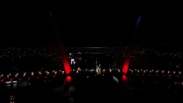 Smooth traffic at night on the Pachuca cable-stayed bridge with the Miguel Hidalgo monument illuminated. Drone orbits in front of the monument