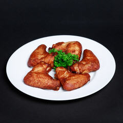 Crispy fried chicken wings coated in paprika, served on a white plate on a dark background, garnished with a sprig of parsley