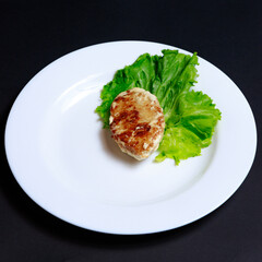 Chicken Cutlet on a White Round Plate with Lettuce Leaves
black background 