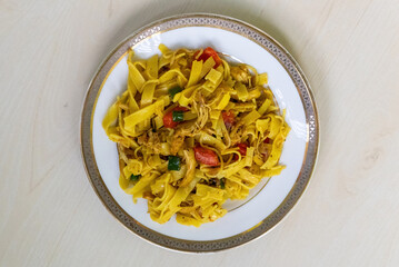 Tasty chicken flat noodles on a white ceramic plate, on a light wooden surface. Top view.