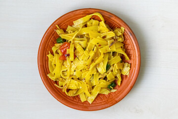 Homemade yummy chicken flat noodles on a traditional clay plate on a light wooden surface. Top view.