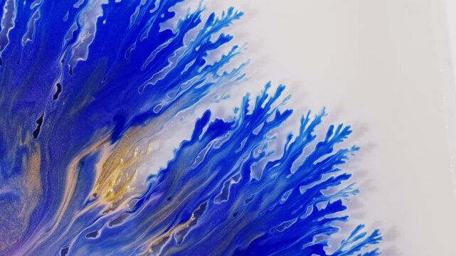 Blue swirls in an acrylic pour painting create intricate patterns on a white background. The fluidity of the liquid paint creates delicate lines that resemble fractal structures.