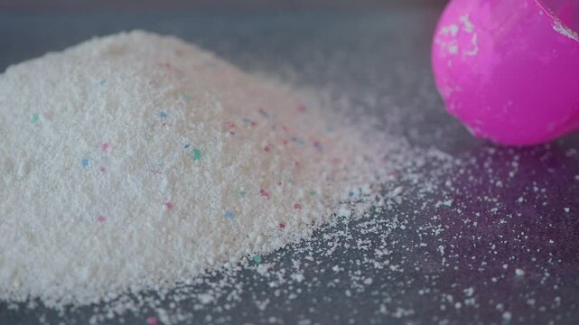 Measuring laundry detergent with a bright pink scoop