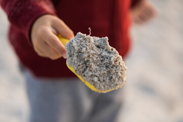 a child toddler holding a yellow shovel full of dry sand on the beach 
