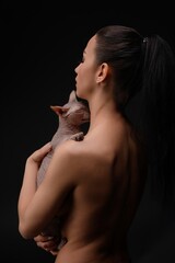 Woman embraces her hairless cat against a dark backdrop in a serene pose