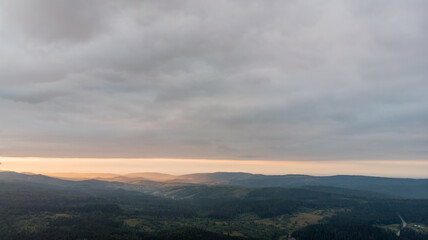 Fototapeta premium Aerial View Of Majestic Mountains Under A Cloudy Sky At Sunset. The Golden Light Illuminates The Peaks, Creating A Stunning Contrast Between The Dramatic Clouds And Rugged Landscape.