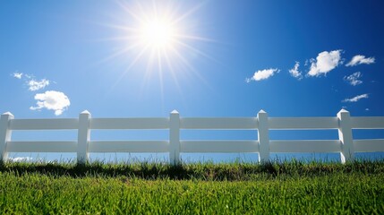 Fototapeta premium A fresh green field meets a classic white wooden fence, glowing under the warm sun with a crisp blue sky above