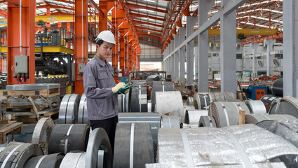 A worker dressed in hardhat and  protective glove, stand in a factory check material while holding...