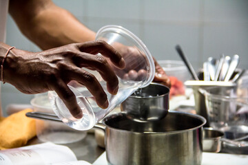 Chef pouring water into a pot in a fine dining kitchen, close-up of skilled hands.