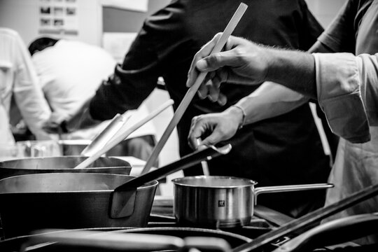 Masterful hands at work: A chef skillfully stirs sauce in a stainless steel pan, captured in a dramatic black-and-white close-up.