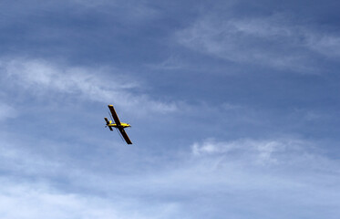 Small single-engine yellow airplane flying against a blue sky with scattered white clouds background