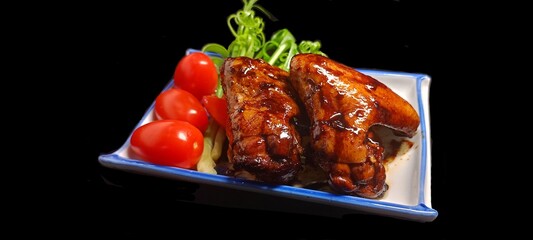 Red chicken wings on a porcelain plate with tomatoes Green onions placed on the side, Thai food, on a black background