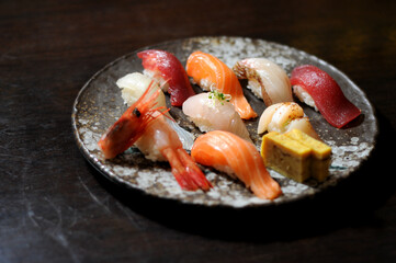  assortment of beautifully arranged nigiri sushi on a rustic ceramic plate, featuring a variety of fresh seafood, including salmon, tuna, shrimp, and tamago, placed on a dark wooden surface.