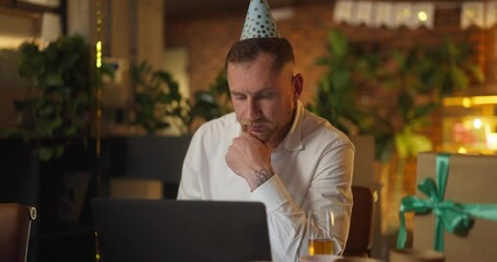 A serious guy in a white shirt and a festive cap works on a laptop after a corporate party in the office
