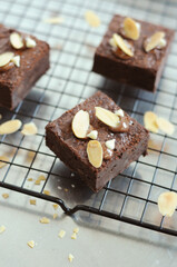  rich, fudgy chocolate brownies topped with sliced almonds and melted chocolate, resting on a cooling rack with scattered almond flakes around them