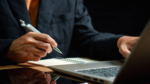Businessman writing note with pen inspired ideas list on notepad while working on laptop computer in office, event planning, Planner plan schedule calendar and reminder agenda