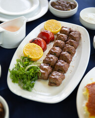 Close-up of delicious and juicy Persian Kebab Kubideh with grilled tomatoes and lemon wedges served on a white platter