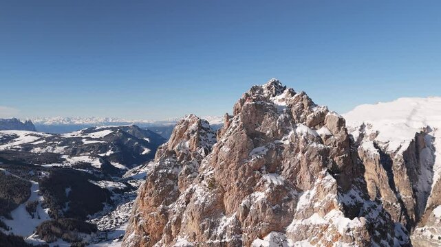 Dramatic winter view of snow-dusted rocky peaks in the Dolomites with distant mountain ranges and valleys under clear blue skies
