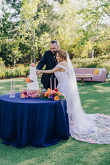 A joyful couple celebrates their love during a wedding cake cutting ceremony in a beautifully decorated garden, surrounded by loved ones and vibrant flowers, creating unforgettable memories for all