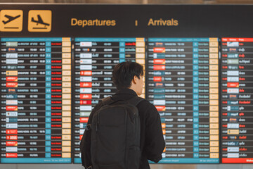 Rear view - Young asian man with backpack and suitcase walking through airport terminal and...