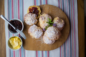 Freshly baked scones dusted with powdered sugar, served on a wooden board, with one scone split open and filled with strawberry jam, creating a cozy and inviting homemade treat presentation.