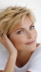 Naklejka premium A woman with short, blonde hair rests her hand gently on her cheek, gazing at the camera with a soft smile.