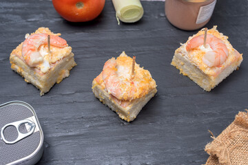 Prawn canape on black slate tray on wooden table with jars, cans of preserves, onion and tomato