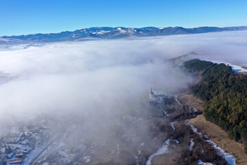 Aerial view of foggy misty mountain village and church tower at winter