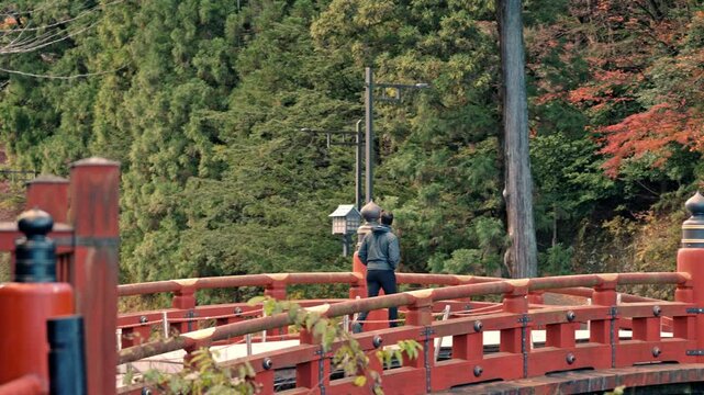 A cinematic video of a man strolling across the iconic Shinkyo Bridge in Nikko, Japan, during the vibrant autumn season.