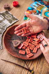 Scandinavian runes in a woman’s hand, tarot cards lie next to her on a wooden table