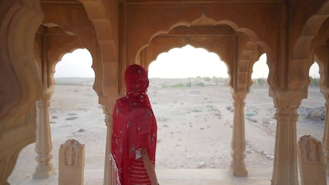 A woman in a saree moves slowly and mysteriously through the sandstone cenotaphs of Bada Bagh, Jaisalmer, India, creating an atmospheric and cinematic scene.