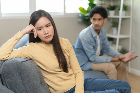 Family problem concept. Tension in relationship between married couple, husband and wife staying sitting separate after quarrel in the living room.