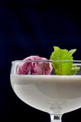 A close-up of panna cotta, showcasing the creamy texture of the dessert and the contrast with the crispiness of the berries. The dessert is topped with a sprig of mint, adding a burst of flavor.
